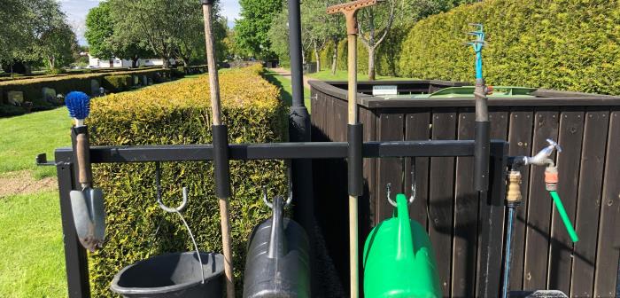 En rad med upphängda trädgårdsredskap; spann, räfsa, grön vattenkanna mm.
