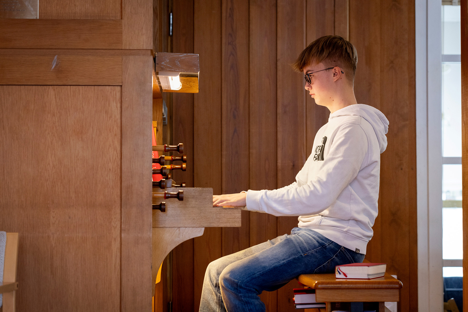 En ung pojke spelar kyrkorgel. Han har vit, långärmad tröja och jeans.