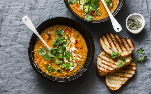 Tallrik med orange soppa, grönt och tre rostade brödskivor vid sidan om.