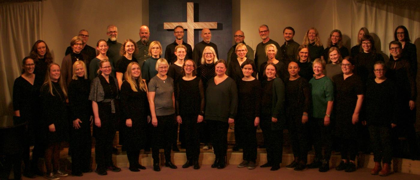 Lutherska Missionskyrkans kör stående i kyrksal framför ett kors. 