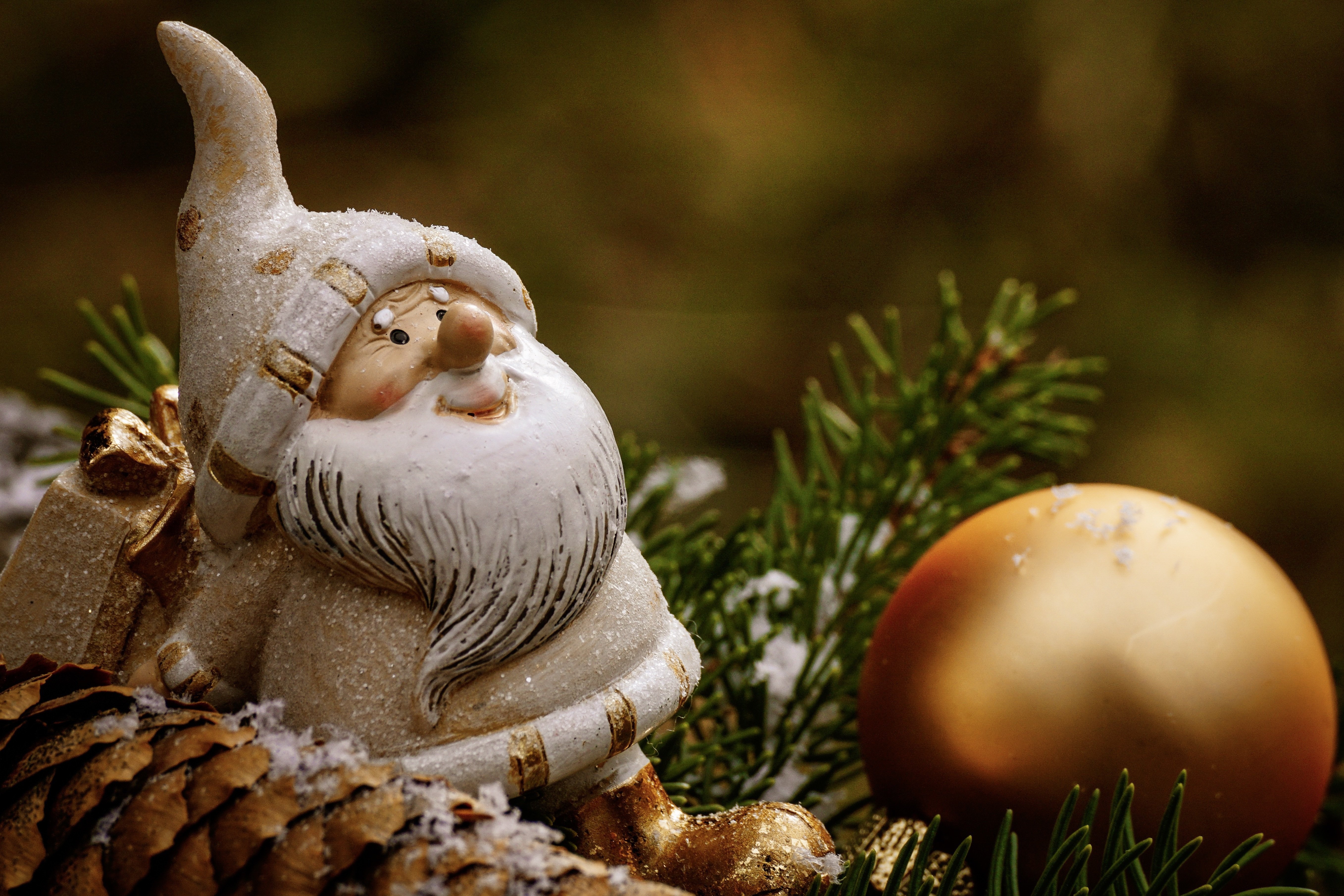 Vit tomte på grankvist och en guldig julkula.