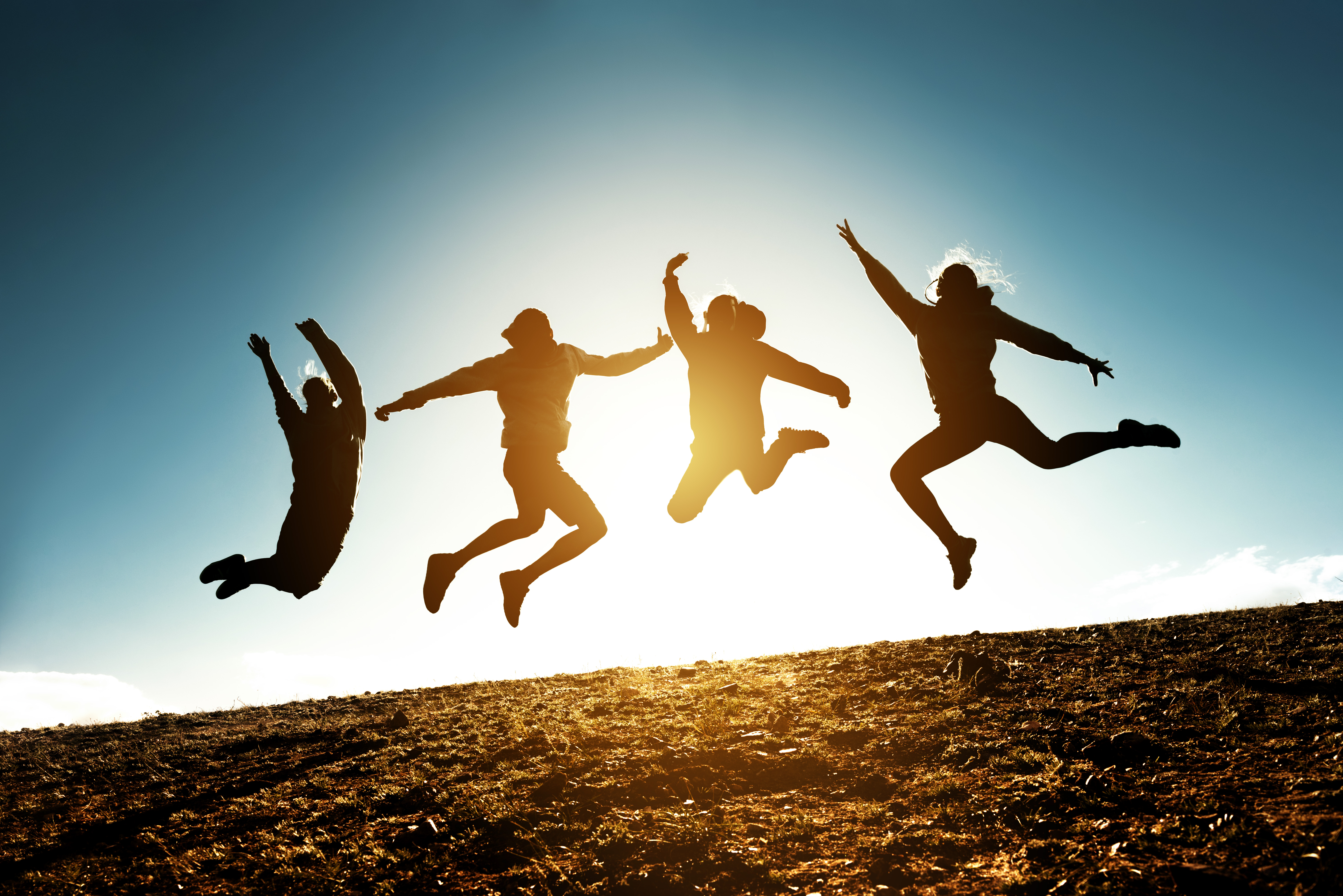 Tonåringar som hoppar, de syns enbart som siluetter mot en ljus himmel.