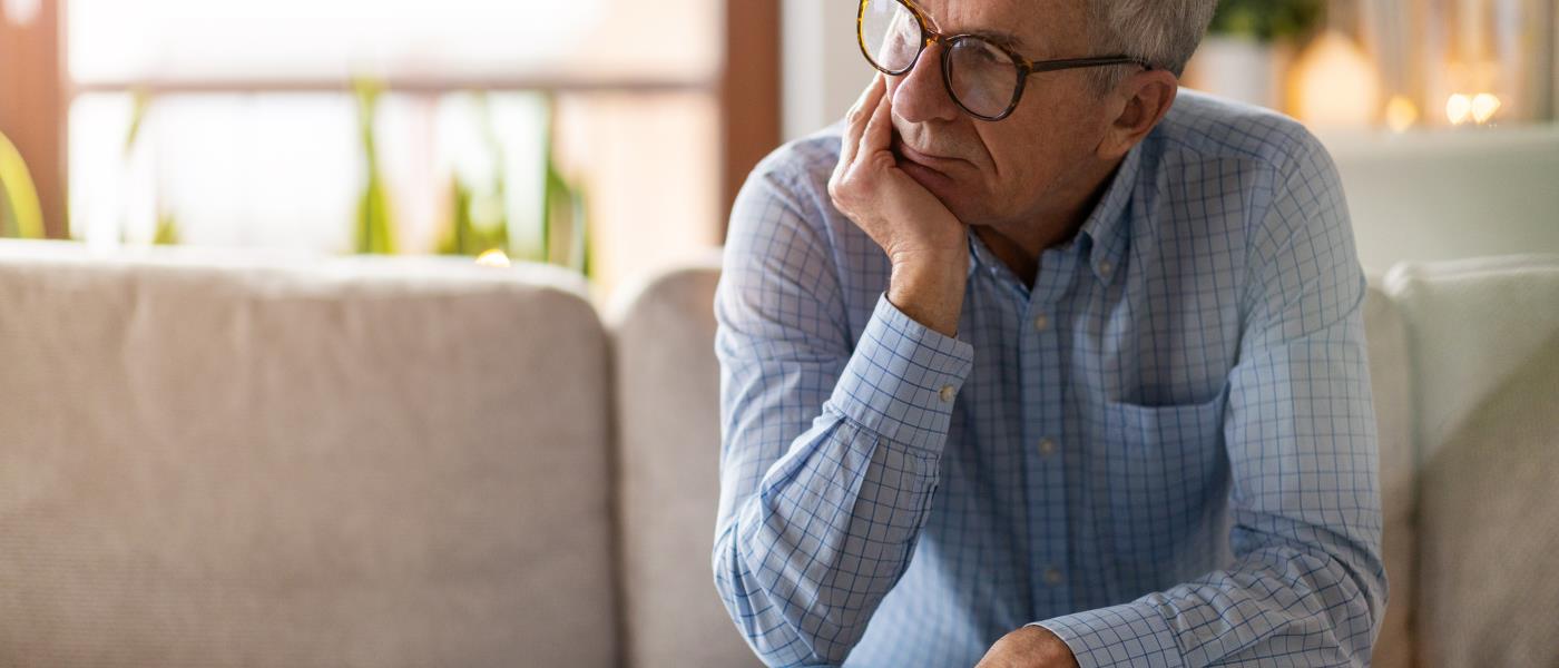 Man sitter på en soffkant och ser sorgsen ut, försjunken i tankar