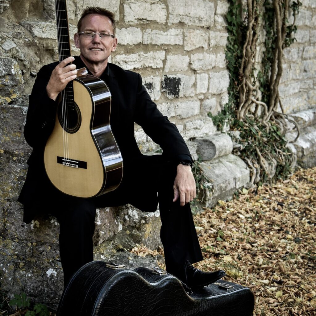 Krister Dahlström sitter på en bänk med sin gitarr.
