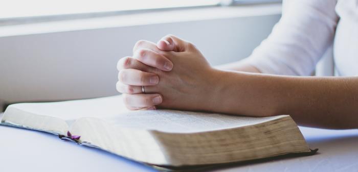 Knäppta händer vilar på en uppslagen bibel.