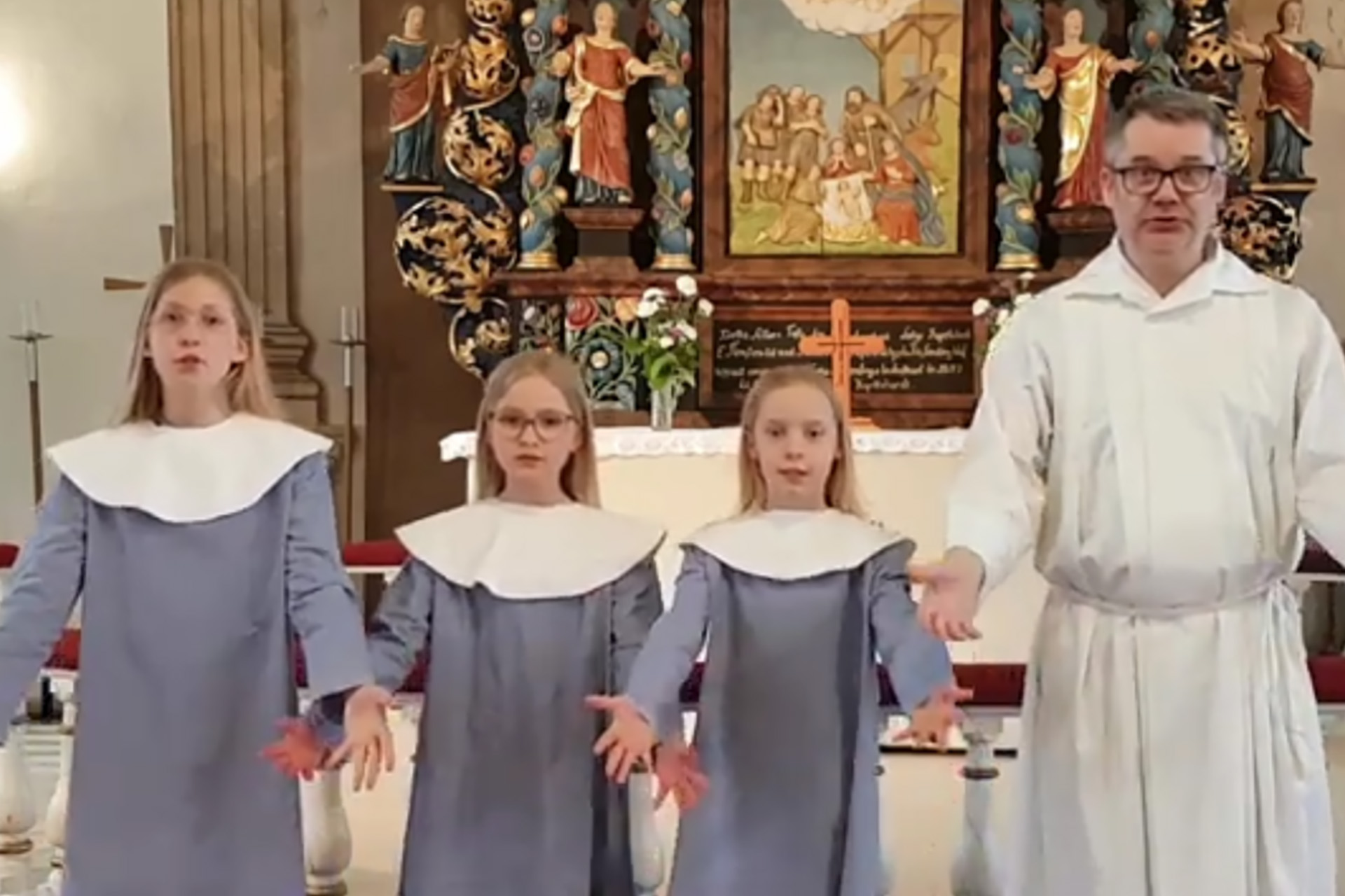 Tre flickor i blå dräkter och en man i vitt som dansar i kyrkan.