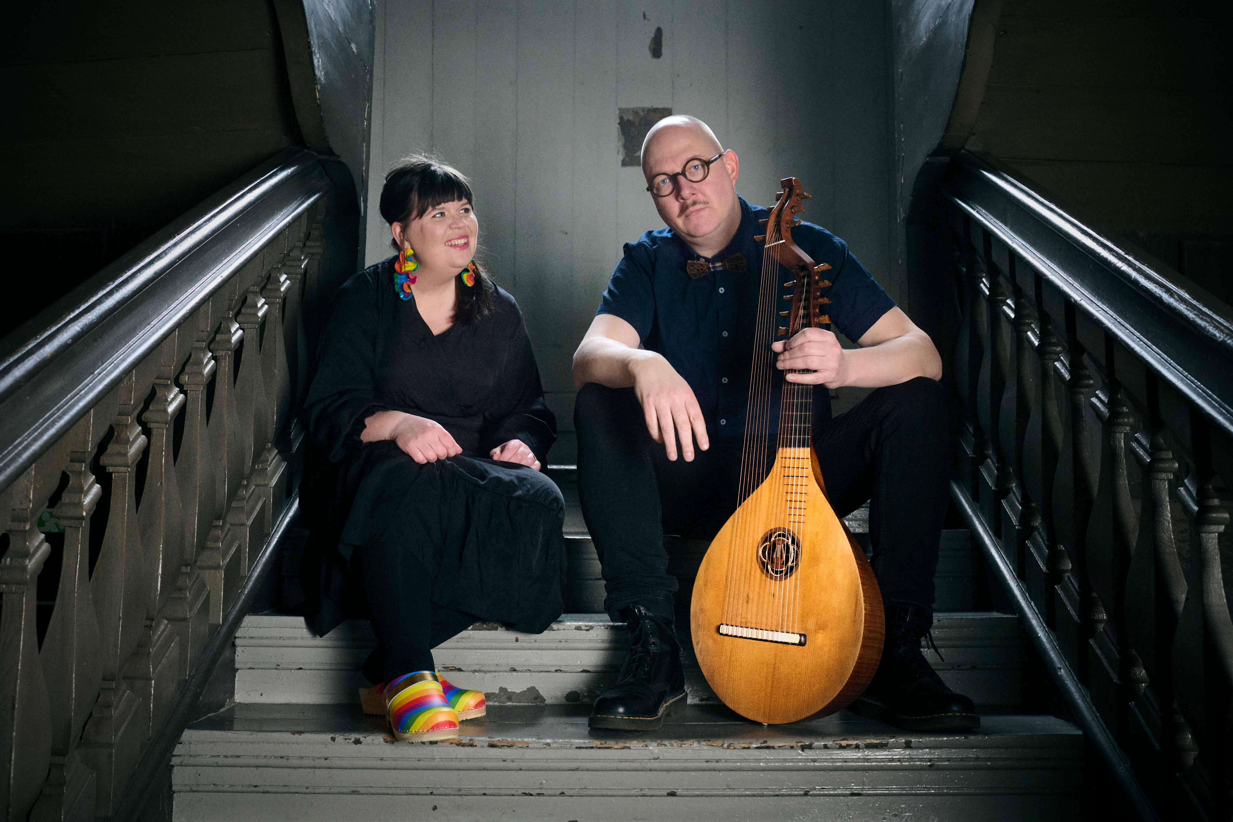 Musikerna Amanda Flodin & Anders Ericson sitter i en trappa. Anders håller en luta i handen.