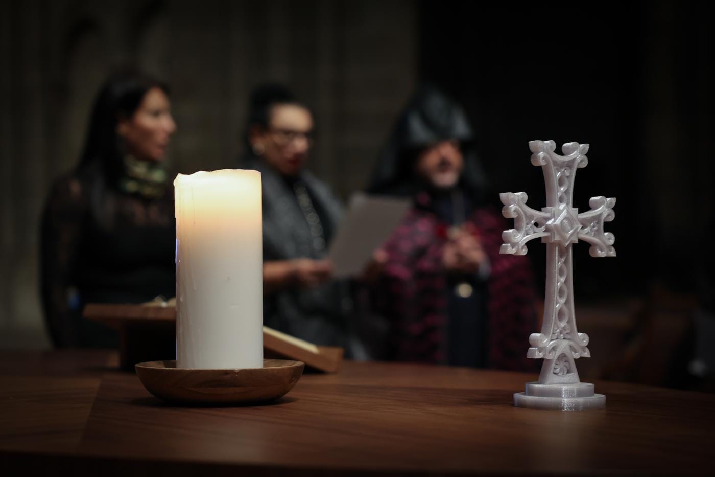 Ekumeniska böneveckan. Ett ljus och ett kors i förgrunden, och tre personer i den suddiga bakgrunden
