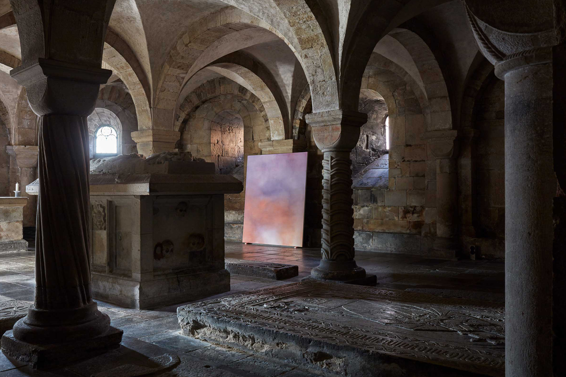 En tavla i lila och röda nyanser står lutad mot en av pelarna i kryptan.