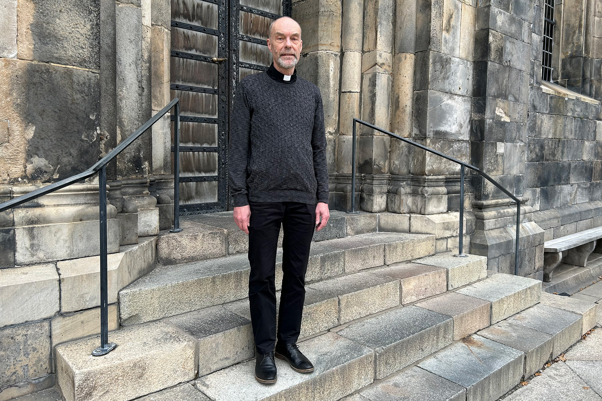 En man klädd i mörka kläder står på trappan till Domkyrkans södra ingång.