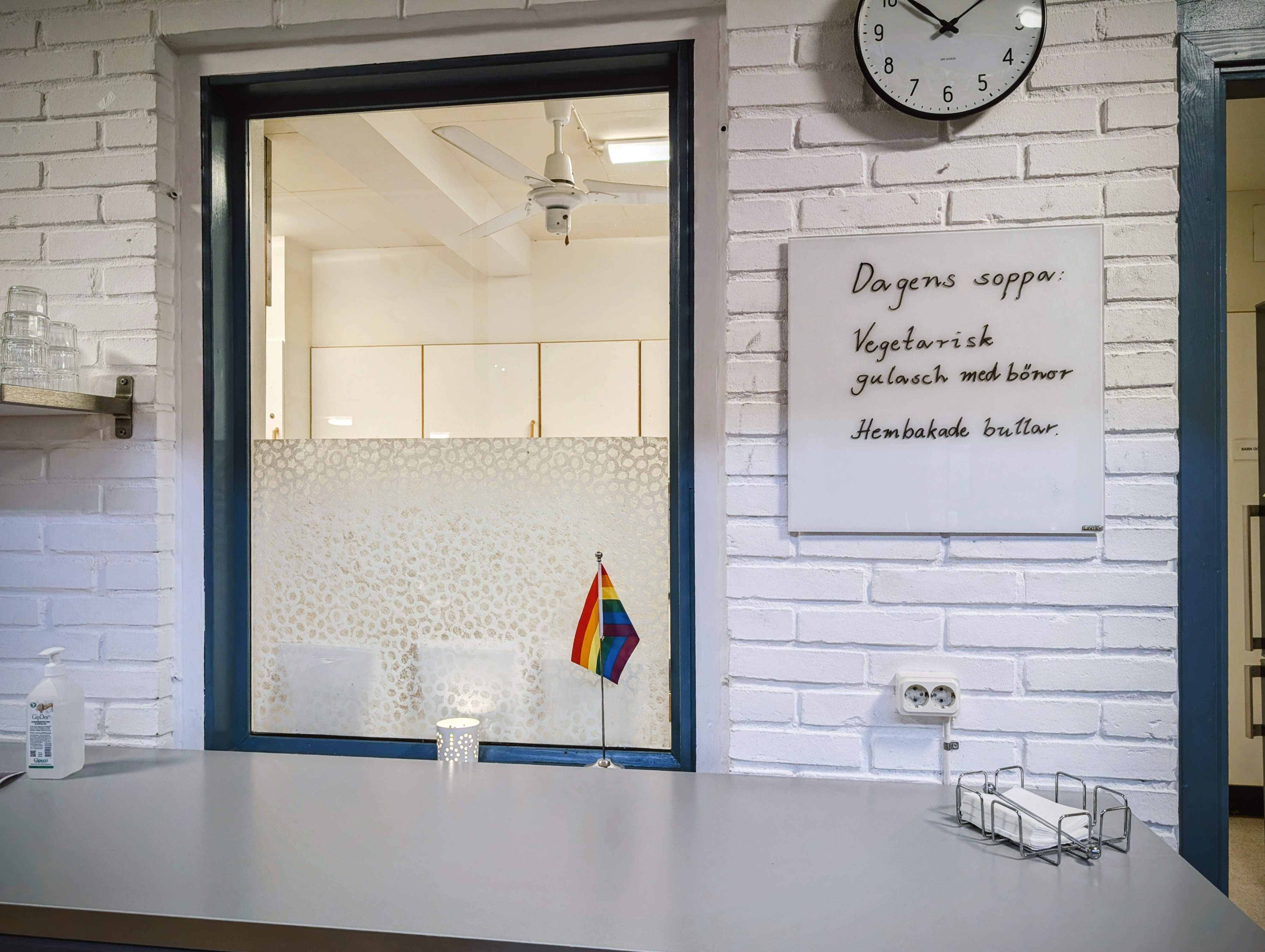 Whiteboardtavla på vitmålad tegelvägg, där menyn för dagen står skriven. Bredvid whiteboarden finns ett fönster