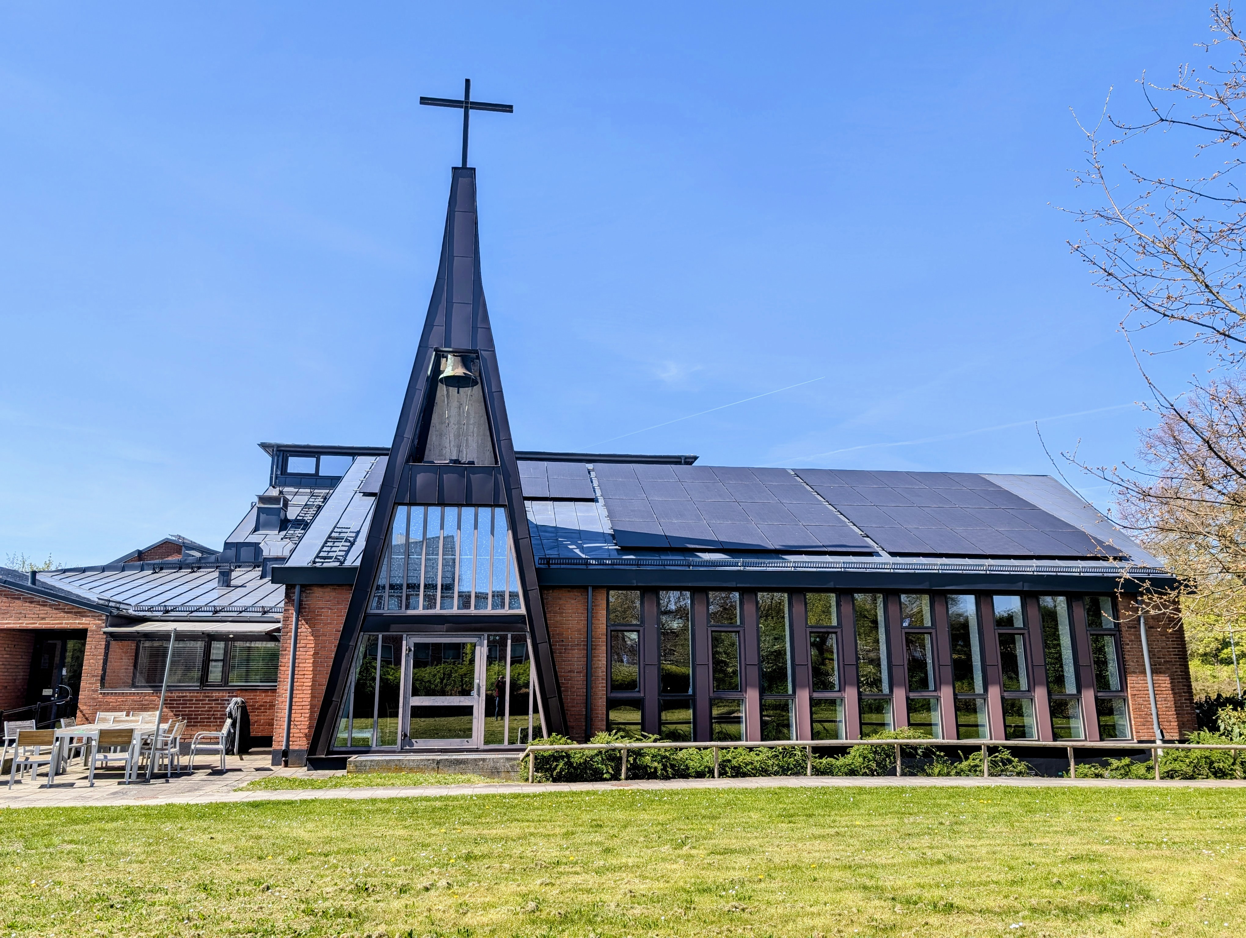 Petersgårdens kyrka med klocktorn och fönsterväggen i fokus. Strålande blå himmel ovanför och en grön gräsmatta syns.