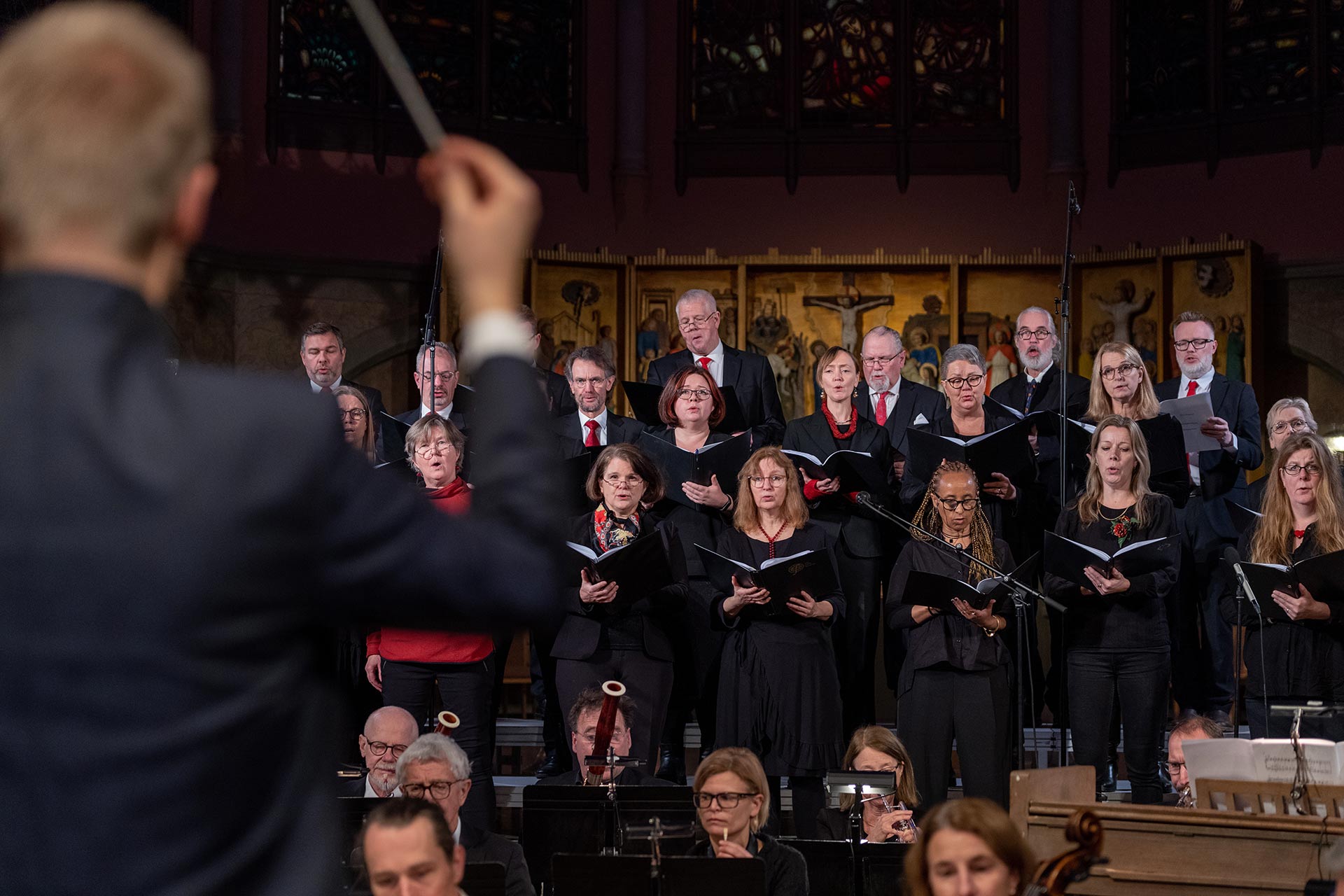 Kör i konsert med dirigent i förgrunden. 