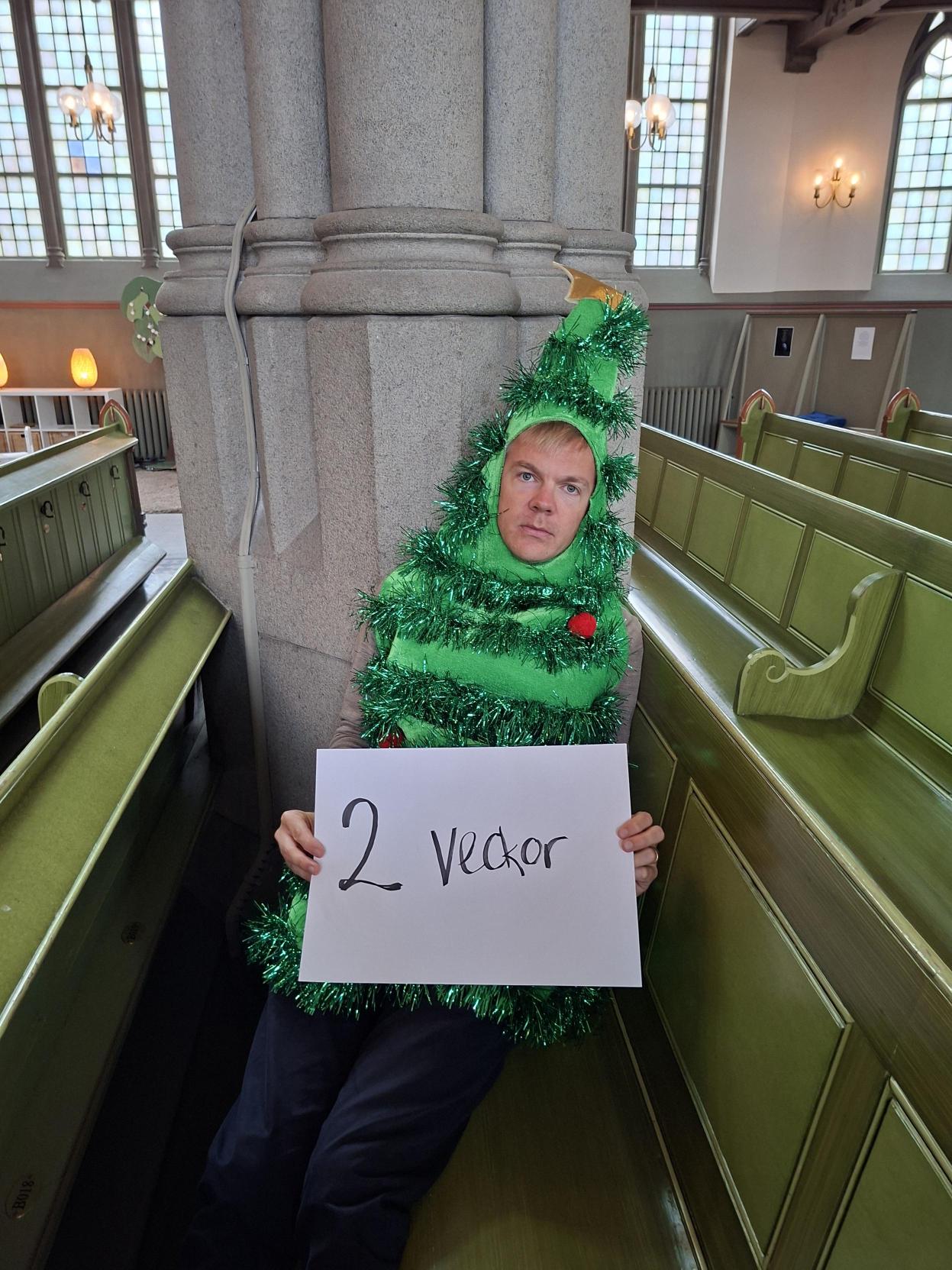 Jakob sittandes på en kyrkbänk med grandräkt på sig med ett papper i händerna där det står "två veckor".