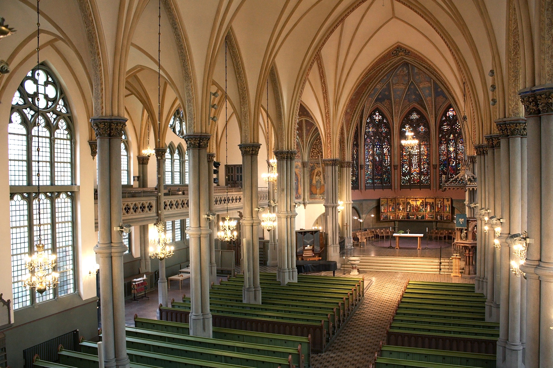 Utsikt ner på kyrkorummet sett från läktaren. Det varma ljuset från kandelabrarna lyser upp det pampiga rummet.
