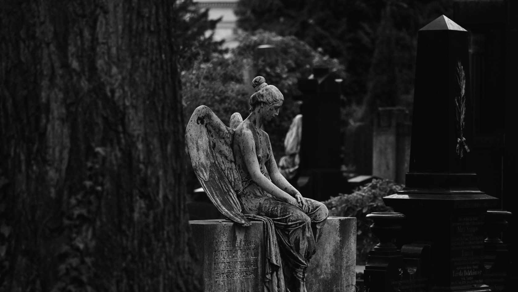 En svartvit bild på en ängel som sitter på en gravsten.