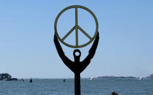 Staty med fredstecken som står vid havskanten. 
