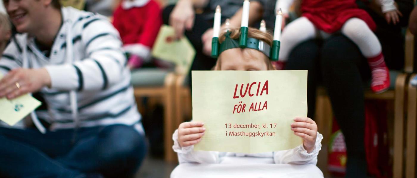 En liten lucia sitter på golvet och läser i ett papper. På pappret står det Lucia för alla.