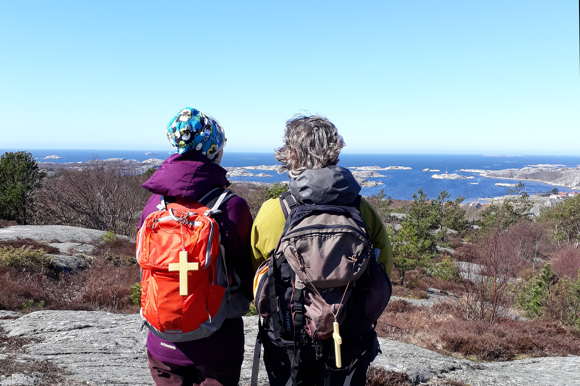Två pilgrimer blickar ut från en klippa över skärgården.