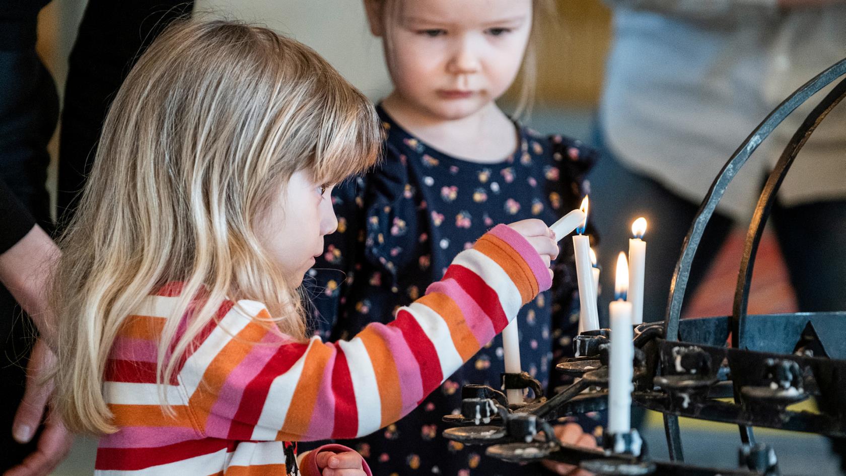 Två barn tänder ljus vid ljusbäraren i kyrkan.