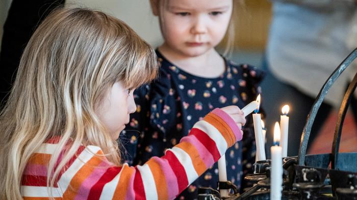 Två barn tänder ljus vid ljusbäraren i kyrkan.