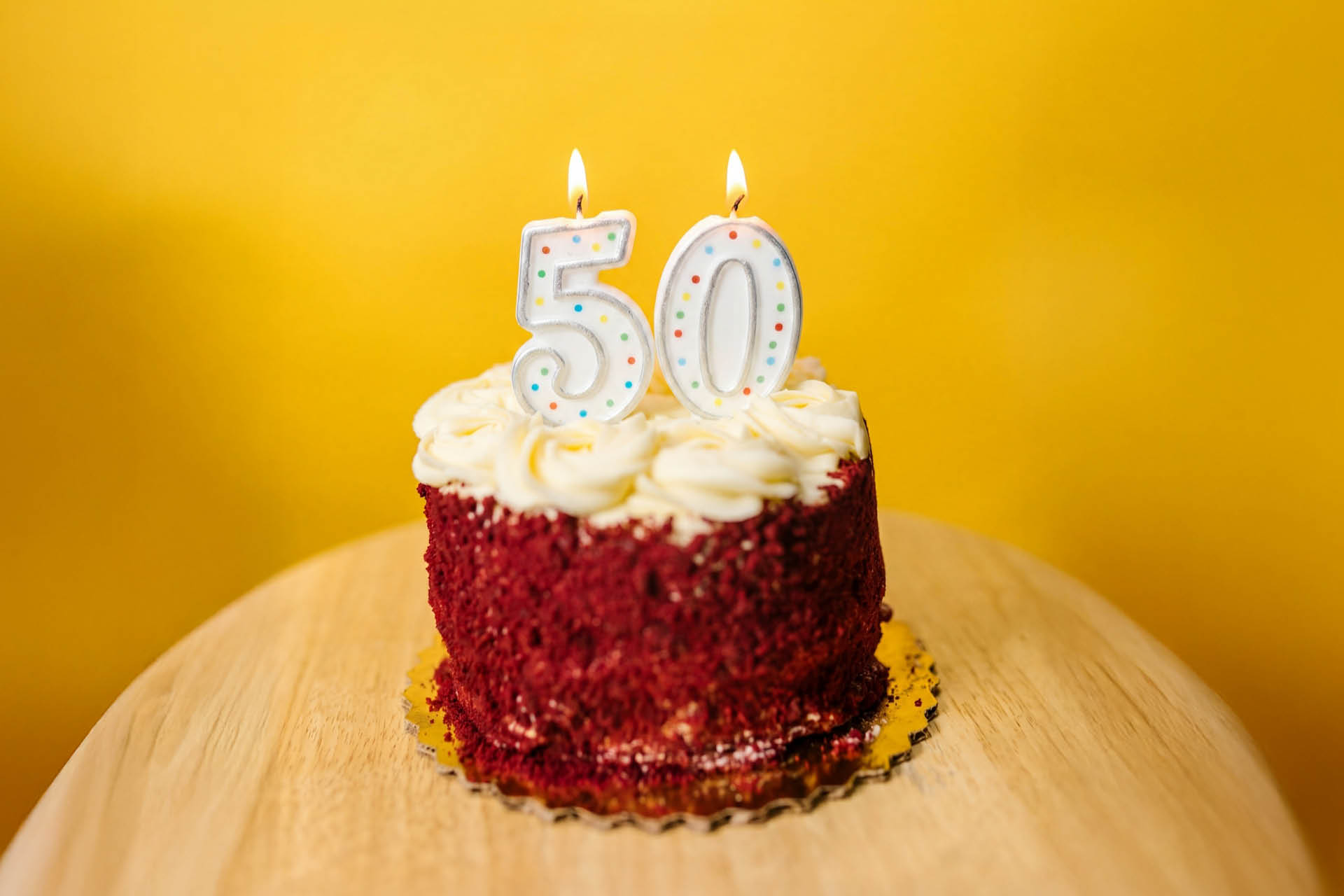 Tårta med sifferljus ("50") på ett bord mot en knallgul vägg