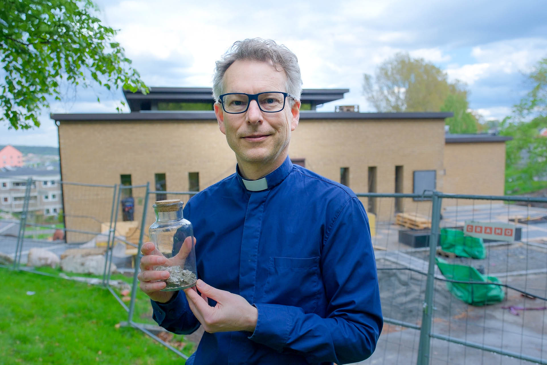 Ola Hedenrud och en burk med skalbanksgrus. Mikaelskyrkan i Askim bakom.