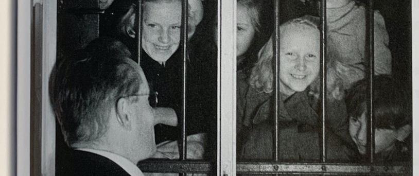 Svartvitt foto av ett dussin leende skolbarn som tittar in genom fönstret mot kyrhoherde Perwe