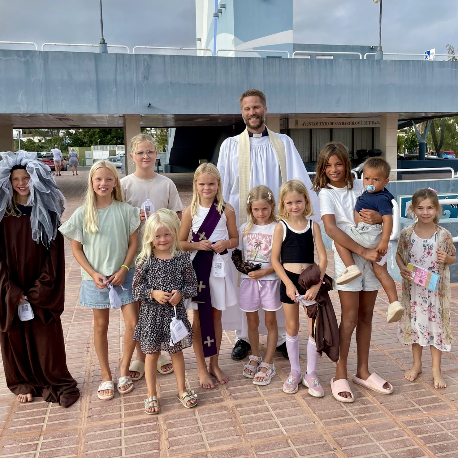 En präst och en grupp barn står utanför Katolska kyrkan i shoppingcentret i San Agustin på Gran Canaria