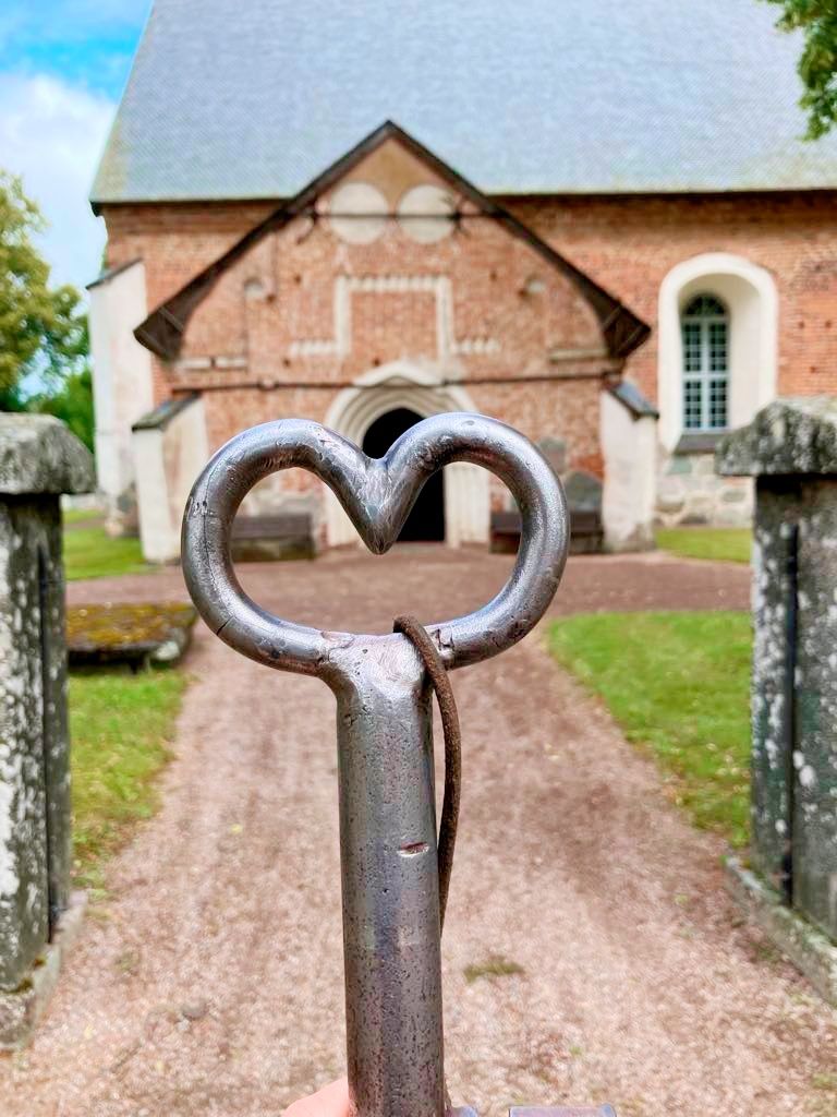 En hjärtformad kyrknyckel hålls i förgrunden till Nysätra kyrka