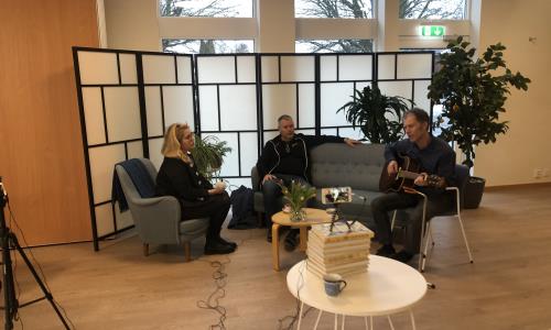 Syntolkning: tre personer sitter i soffgrupp. Ett stort och ett litet kamerastativ syns i förgrunden. Många sladdar.