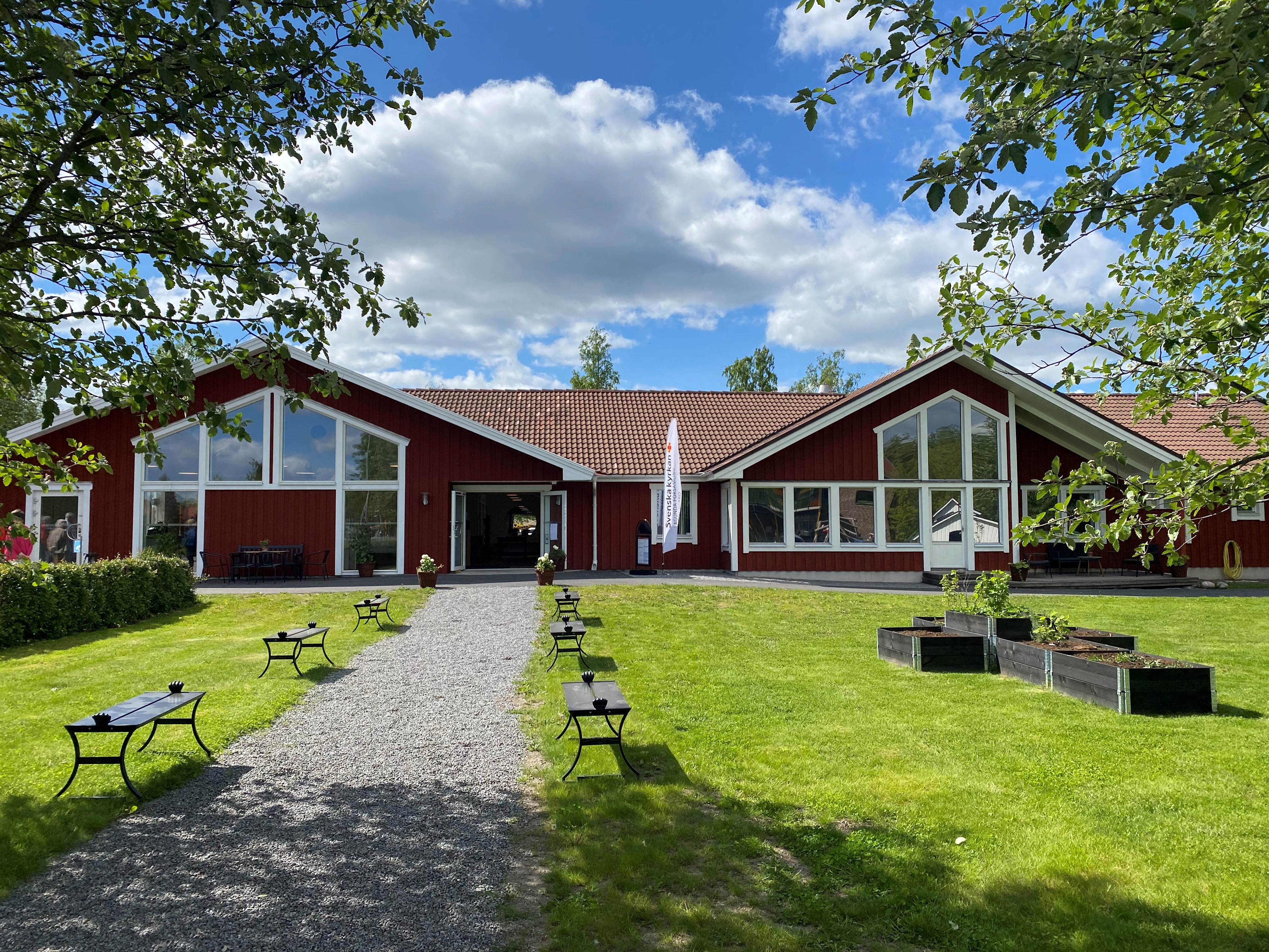 Syntolkning: Röd byggnad med två vinklade tak. Gräsmatta framför. och grusgång in.