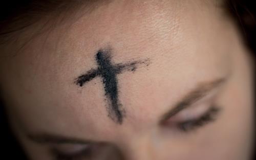 Syntolkning: Ung kvinna med kors tecknat i pannan. Kvinnan blundar.
