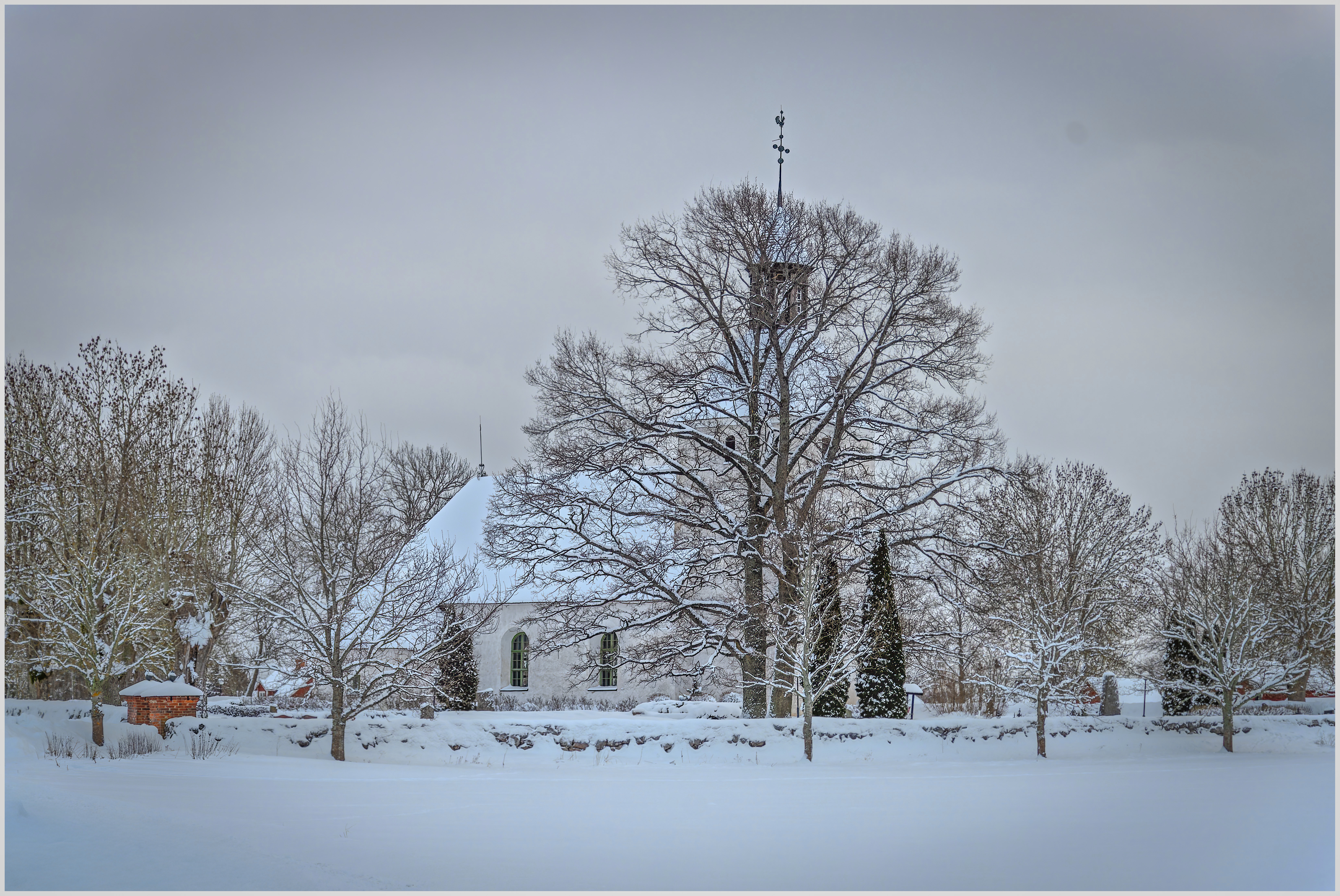 Kyrka i vinterskrud med träd i förgrunden.