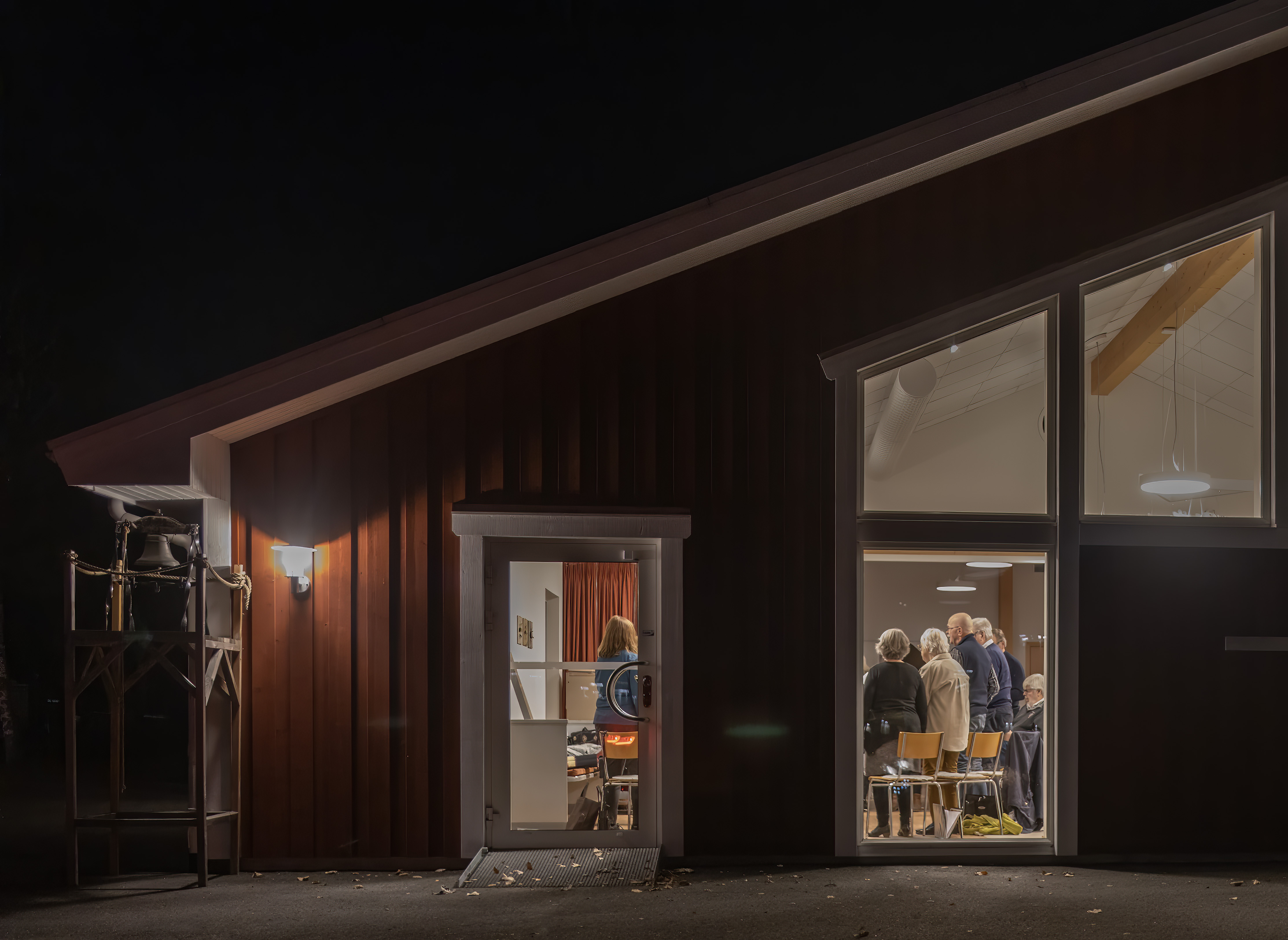 En röd kyrka av trä sedd utifrån där man kan skymta vuxna körmedlemmar.