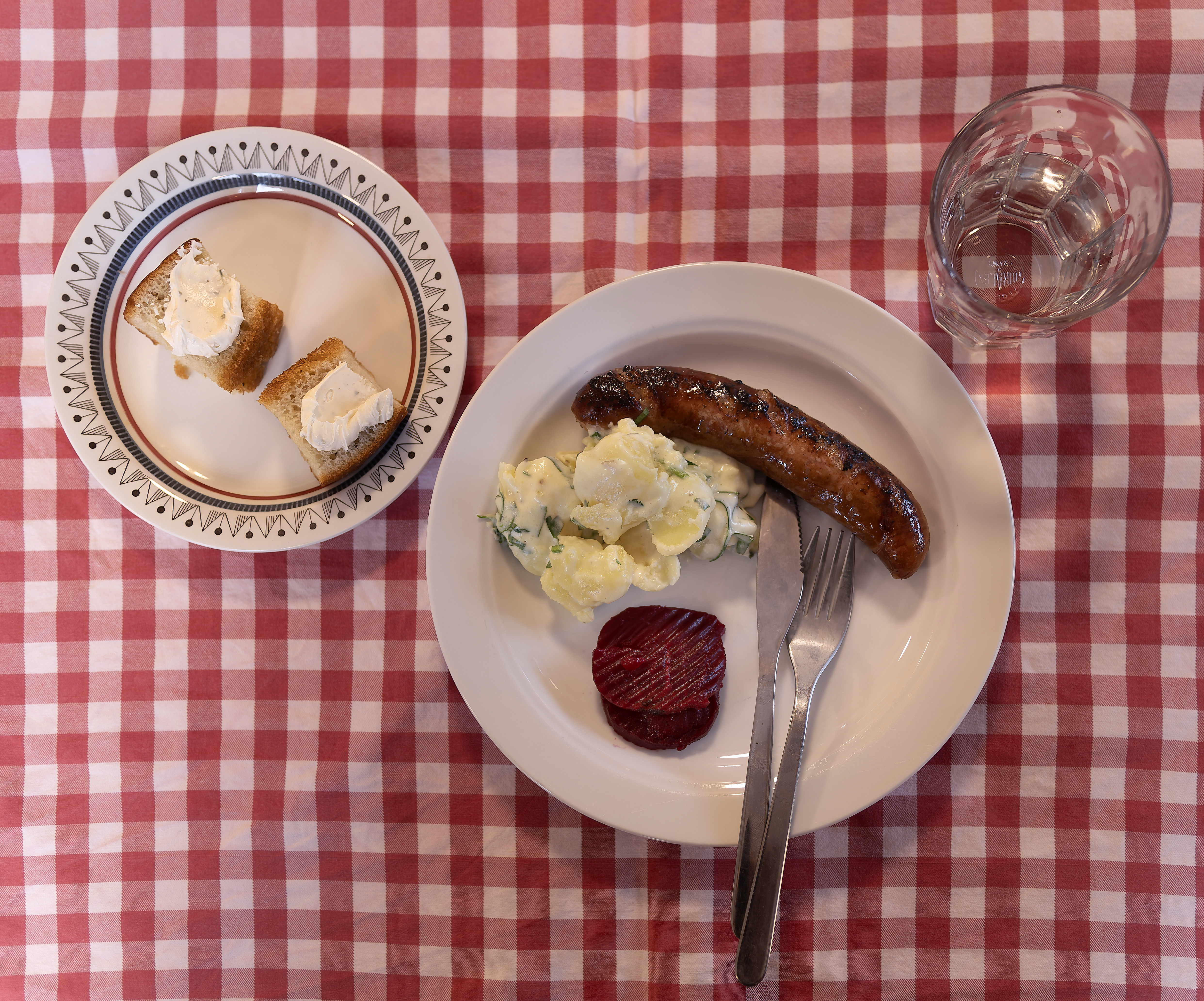 Lunchtallrik, korv med potatissallad och rödbetor, nybakat bröd med vispat smör.