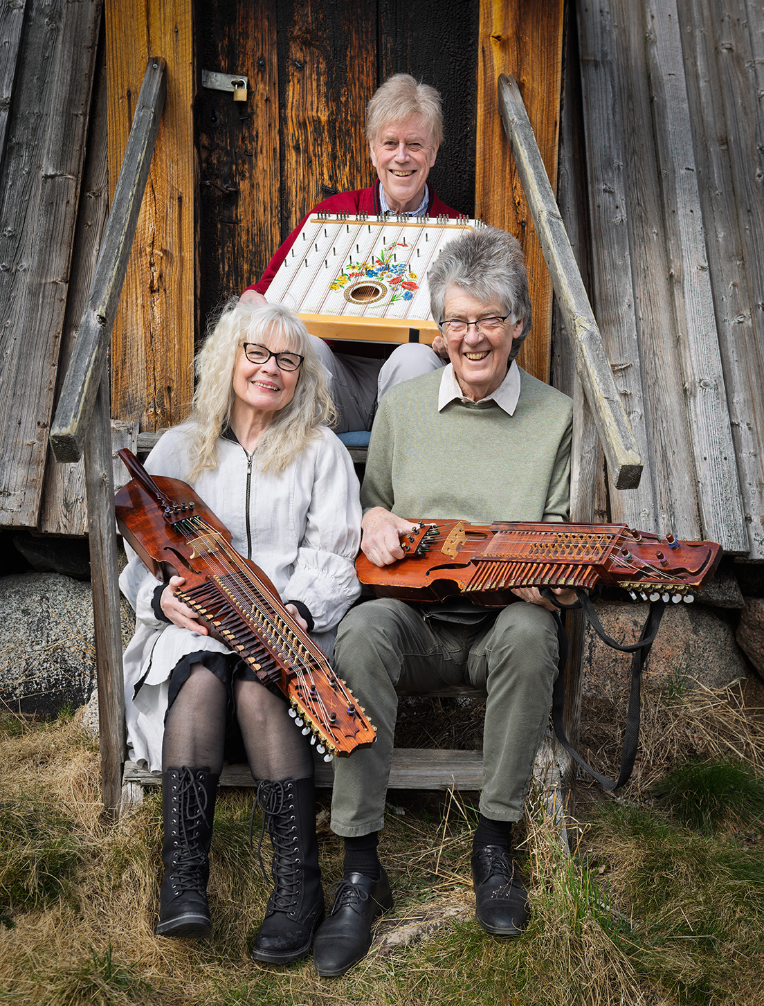 Tre folkmusiker sitter på en trapp och visar sina nyckelharpor