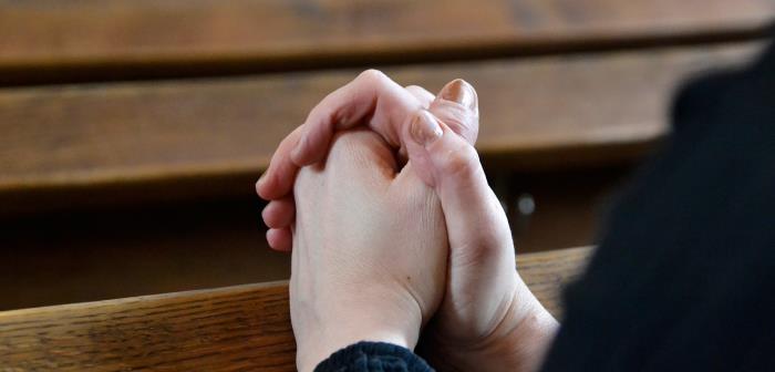Händer knäppta i bön i kyrkbänk.