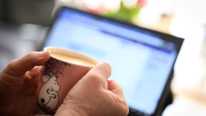 Händer som håller i kaffemugg framför dataskärm