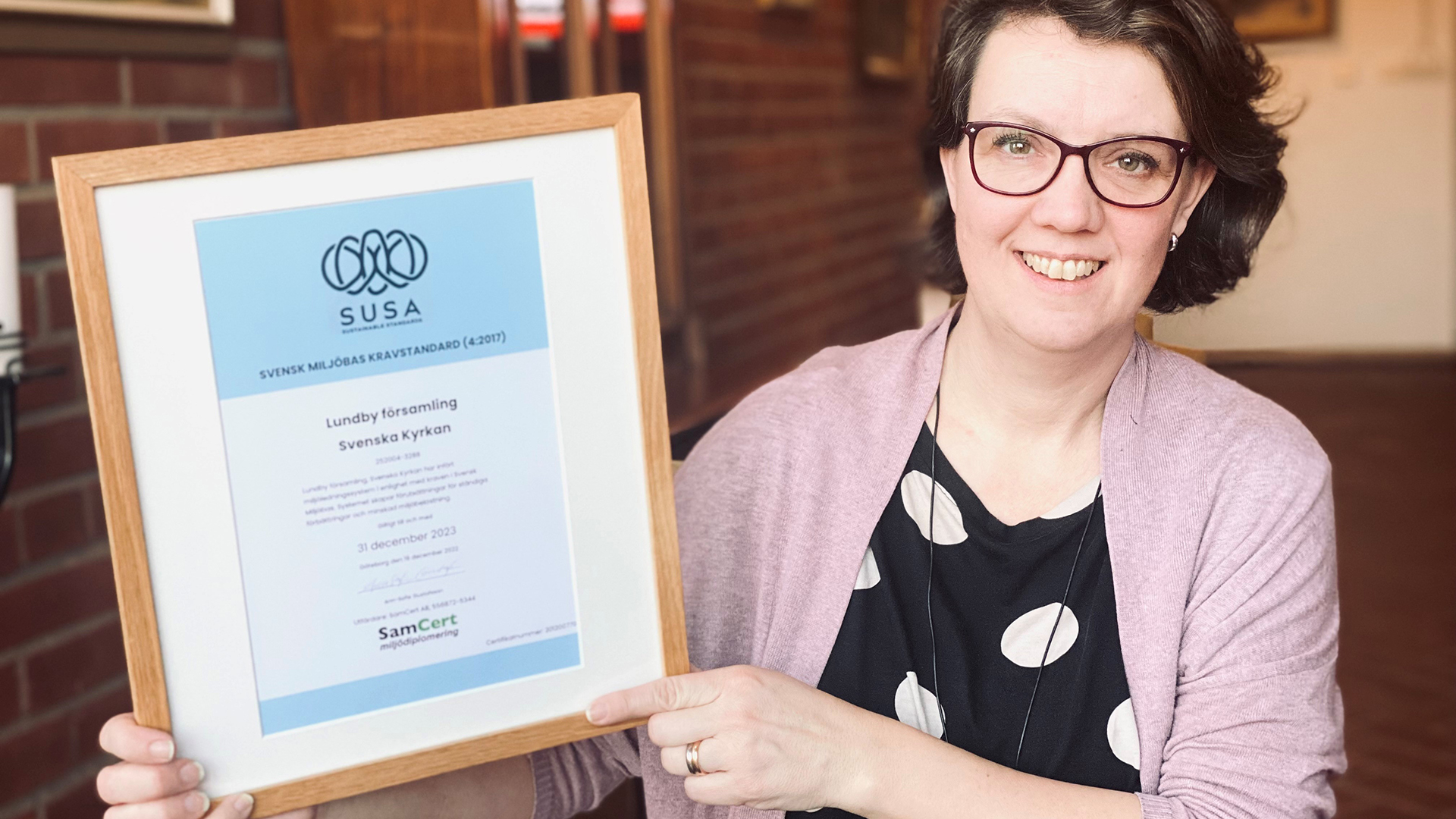 Kvinna visar upp ett inramat diplom för miljödiplomering.