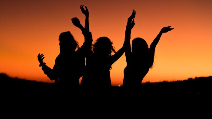 Siluetter av tre tjejer med uppsträckta armar. I bakgrunden syns solnedgången.