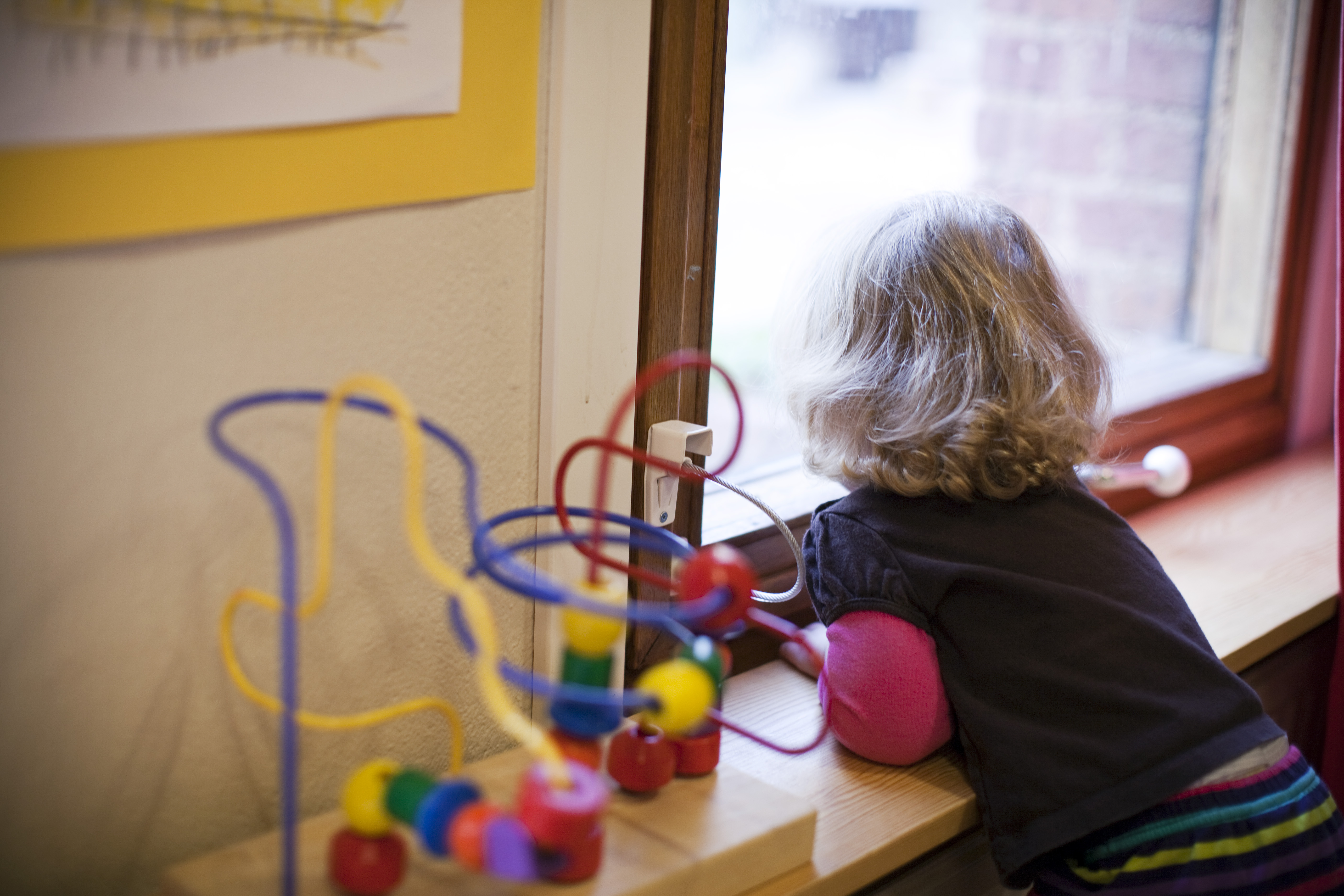 Barn står och tittat ut genom fönstret. Bredvid hen står leksaker