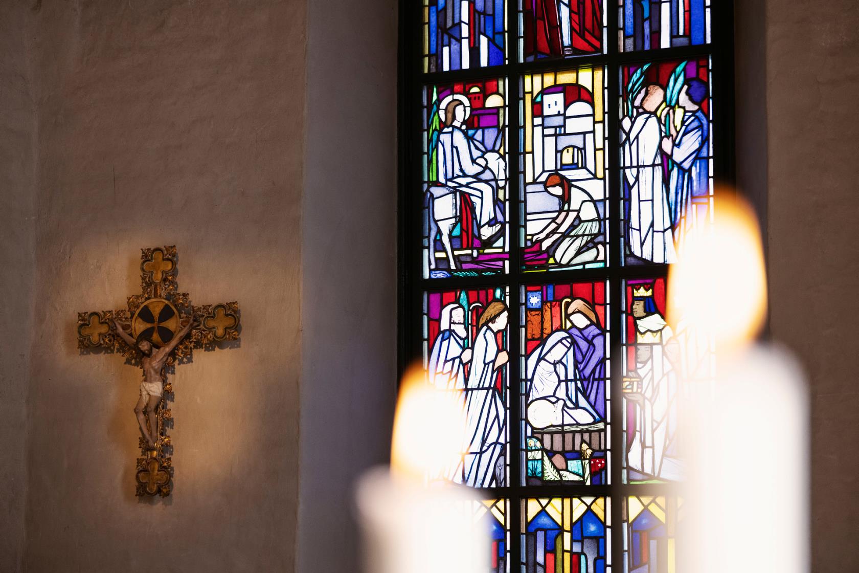 Krucifix med ett kyrkfönster bredvid och ljus i förgrunden