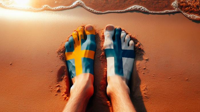 Två fötter på en strand den vänstra målad som svenska flaggan och den högra som finska flaggan