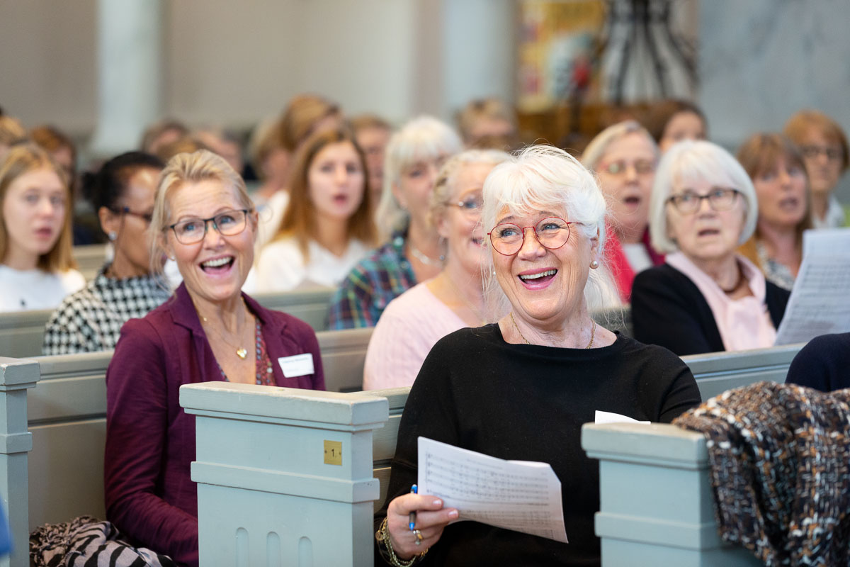Grupp med kvinnor som sitter på kyrkbänkar och sjunger