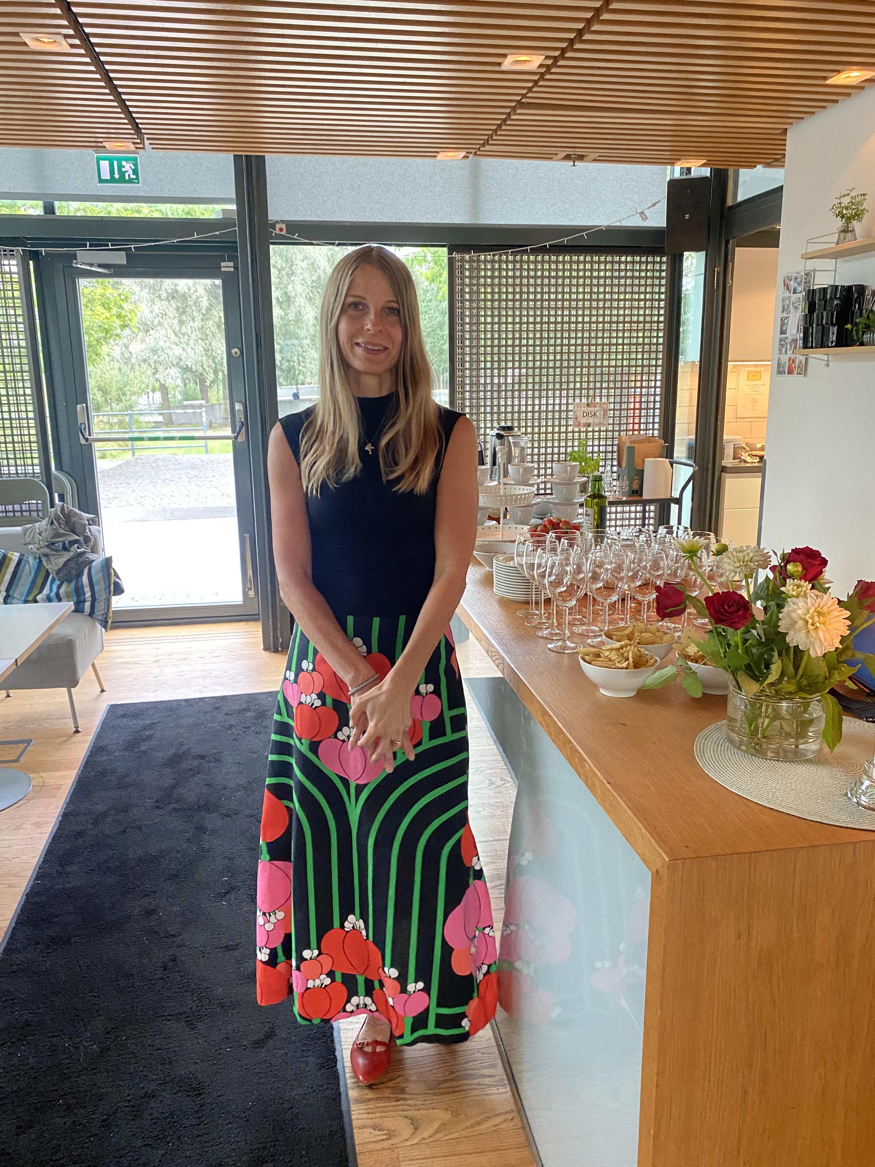 Susanna Kaarle står bredvid ett bord med vinglas, blommor och tilltugg.