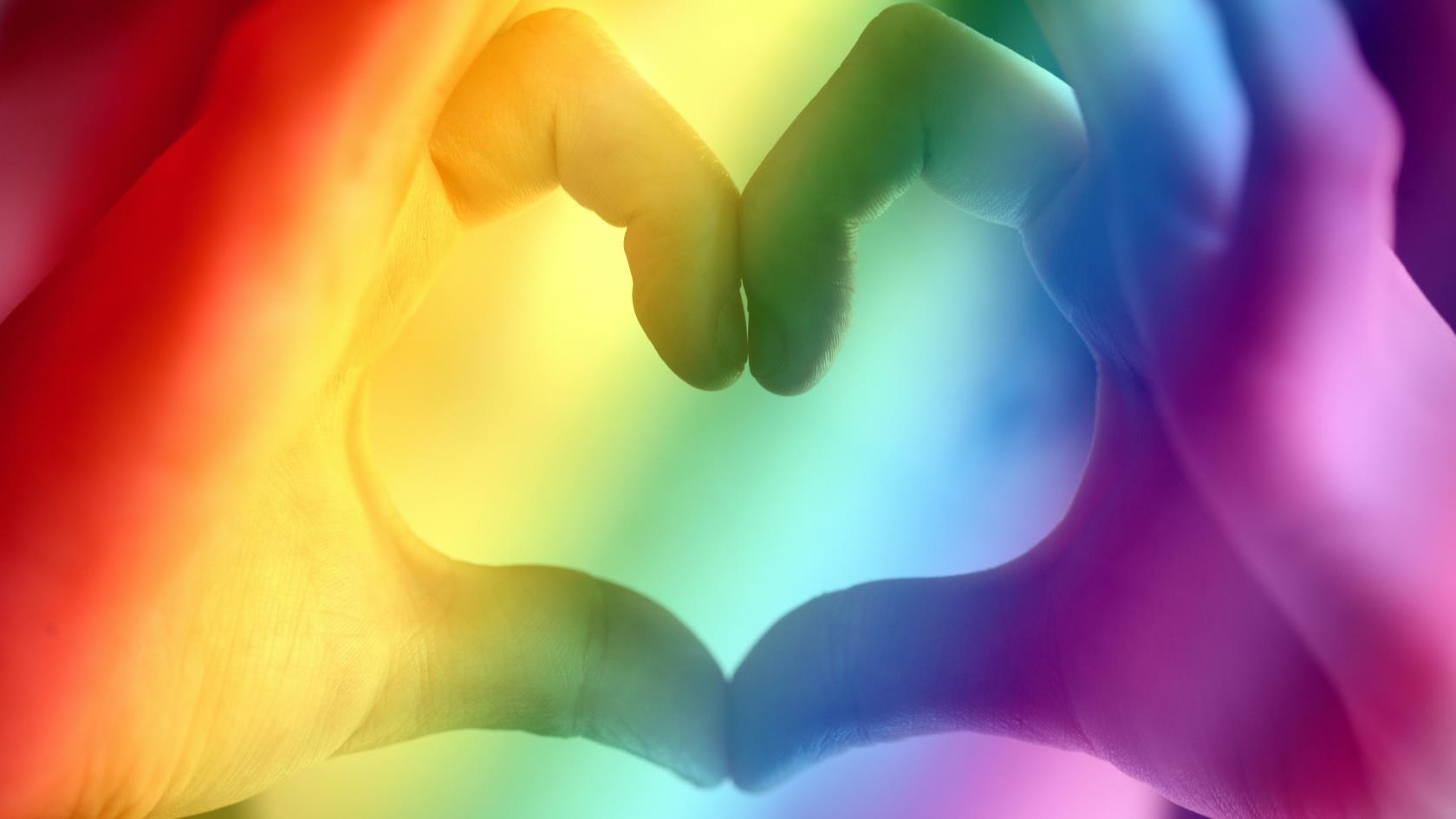 Två händer som bildar en hjärtform. Bilden är i regnbågens färger.