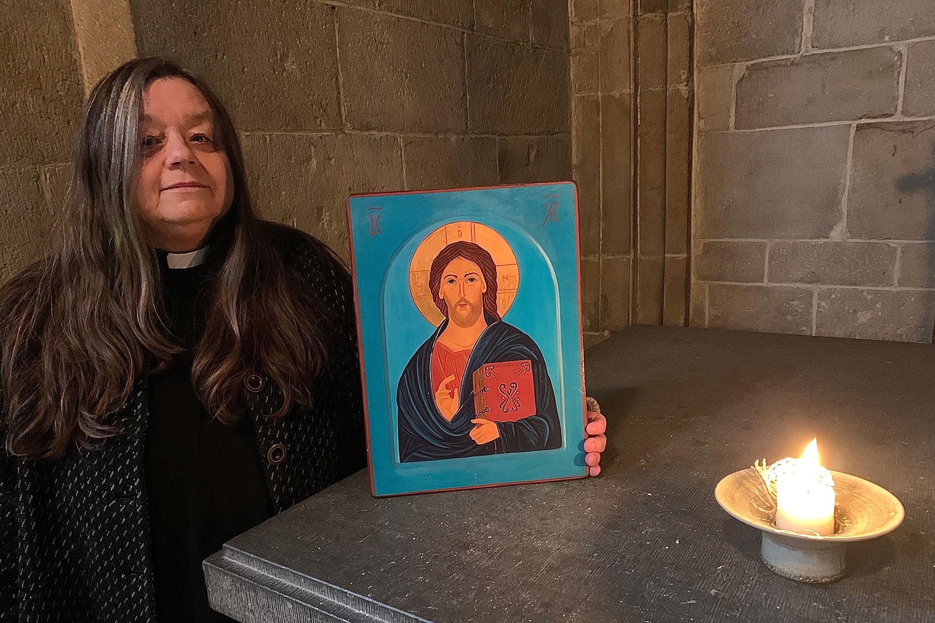 Kvinna invid ett altare med en ikon och ett tänt ljus.