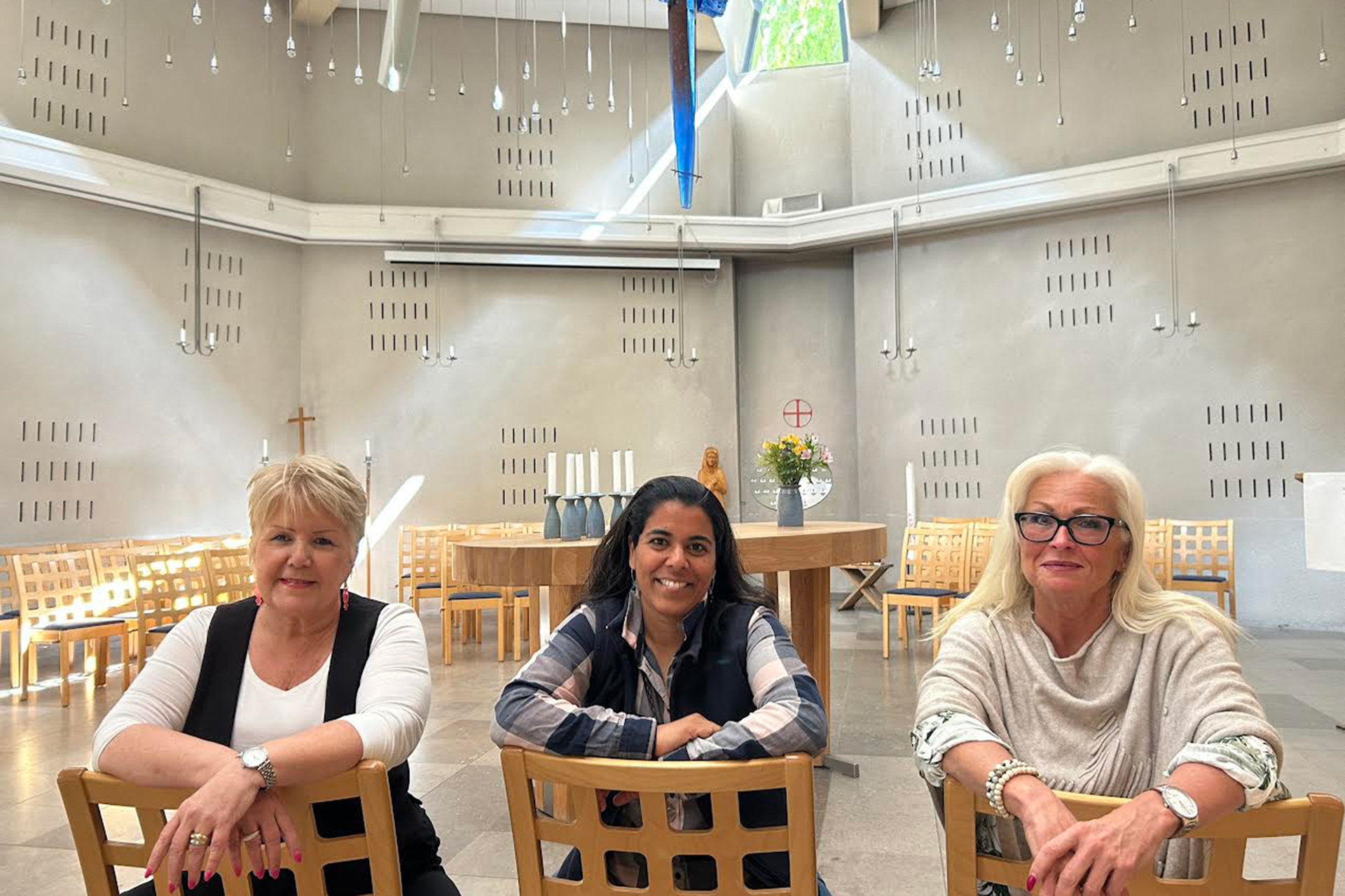 Tre kvinnor sitter på bakvända stolar i ett kapell.