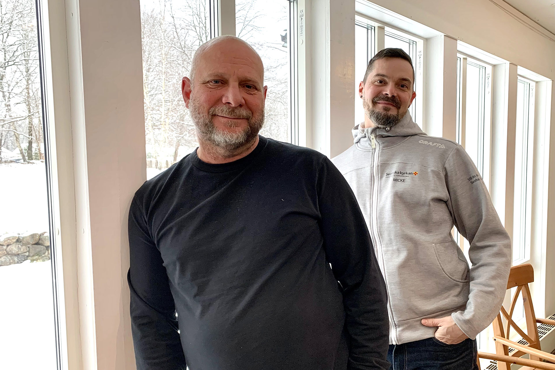 Två män står lutade mot en fönstervägg.